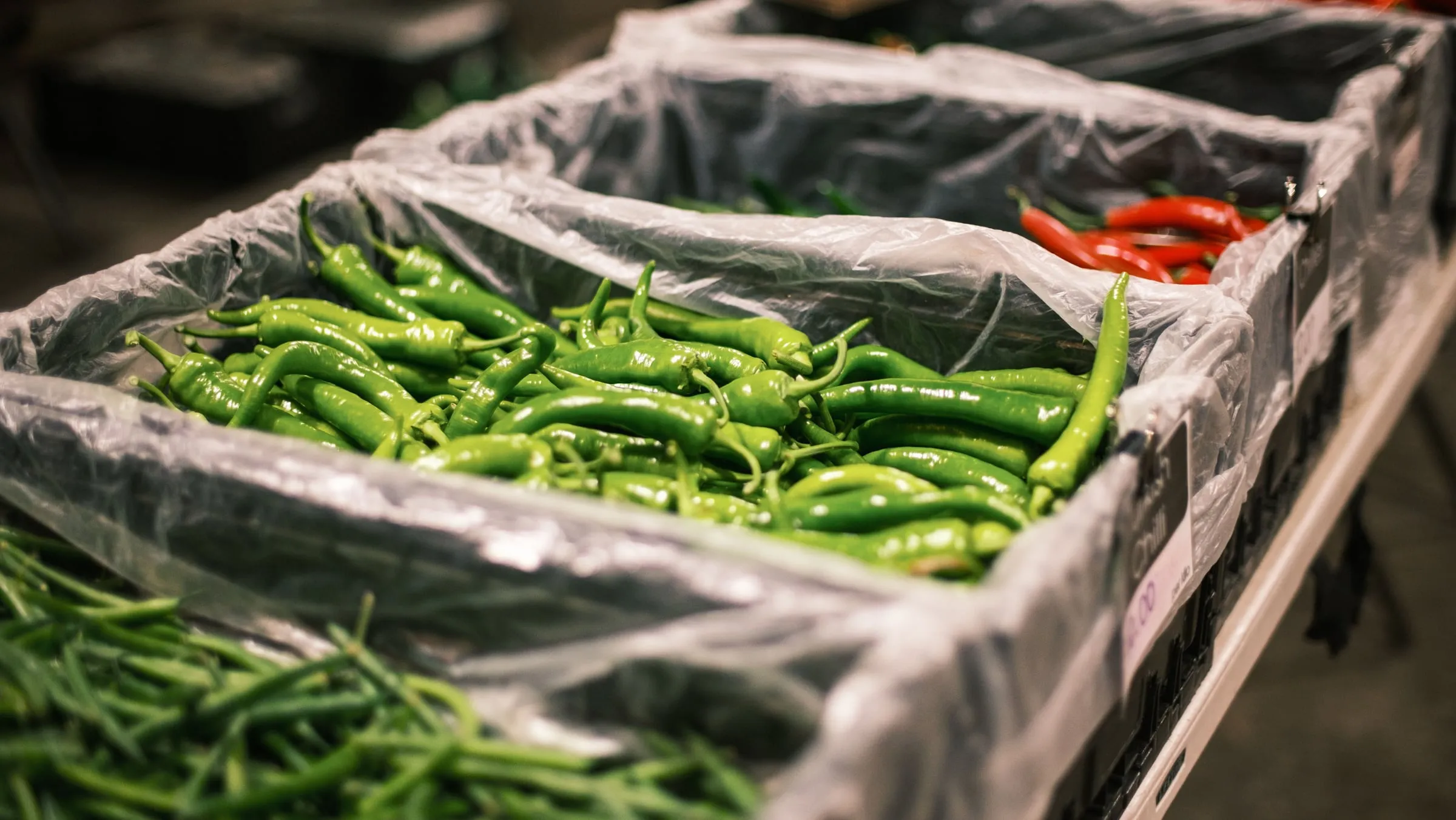 Green chillies packed into lined crates at a market, a crate of red chillies behind them