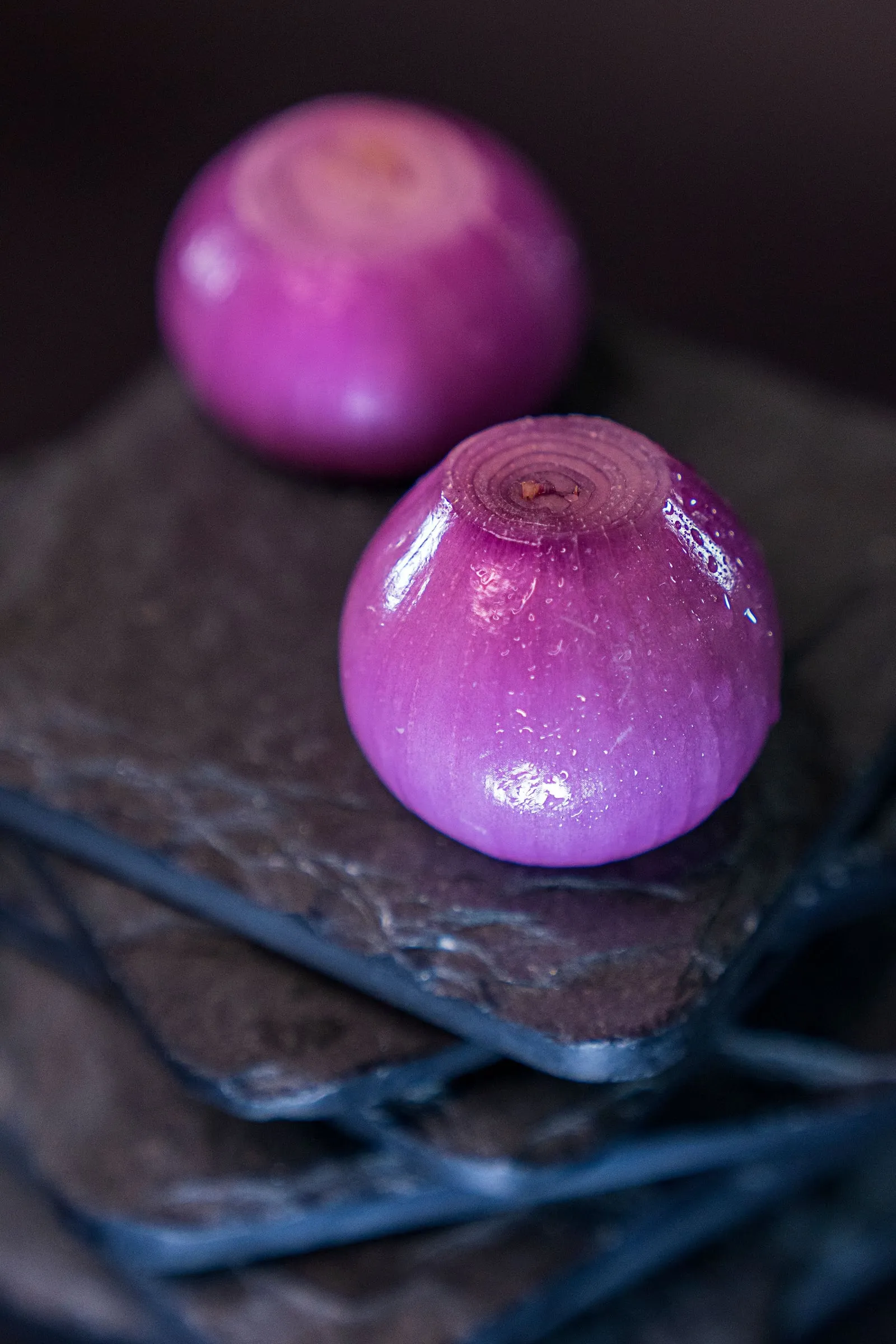 Two red onions on a slate slab, the nearer one beaded with water